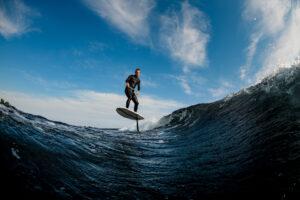 Mann, der gekonnt auf einer Welle mit E Surfboard reitet, bzw. surft.